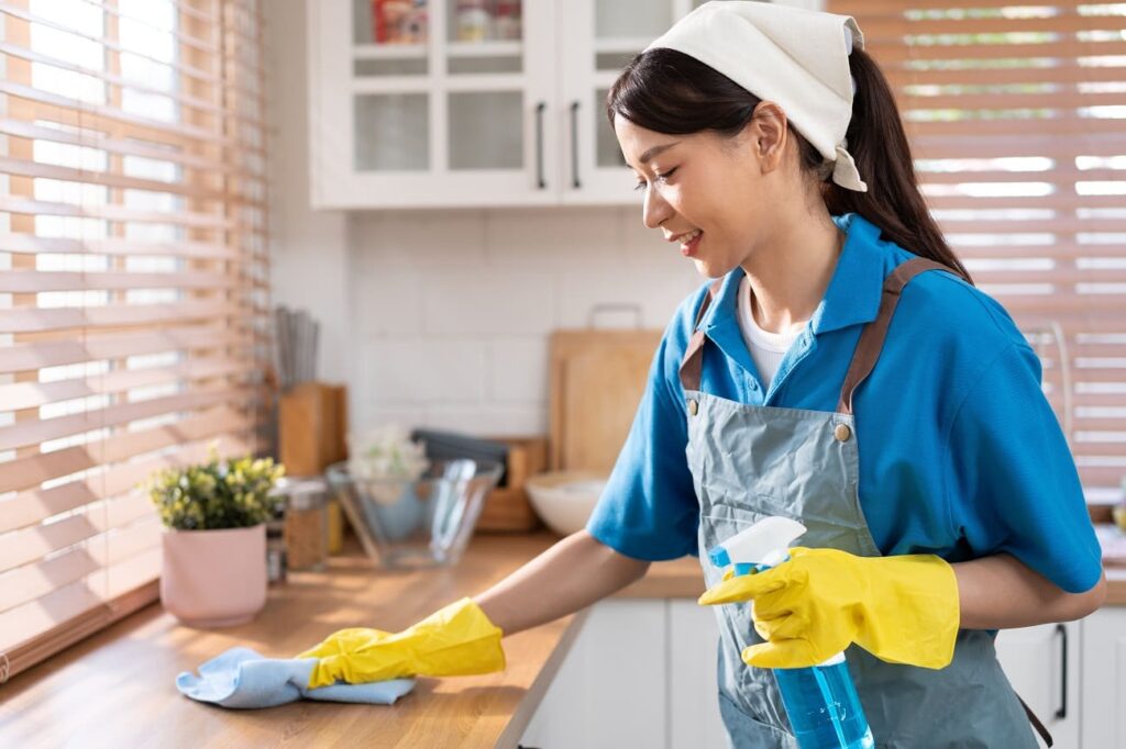 Woman wearing gloves cleaning a kitchen counter with spray
