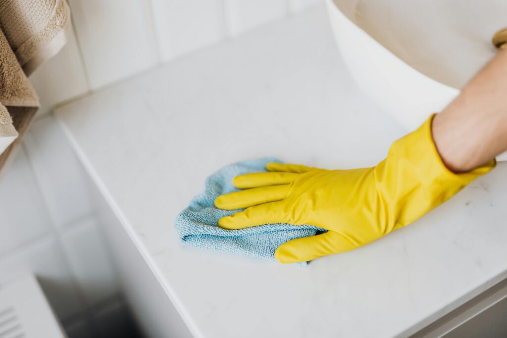 Person cleaning a bathroom counter with yellow gloves and blue cloth